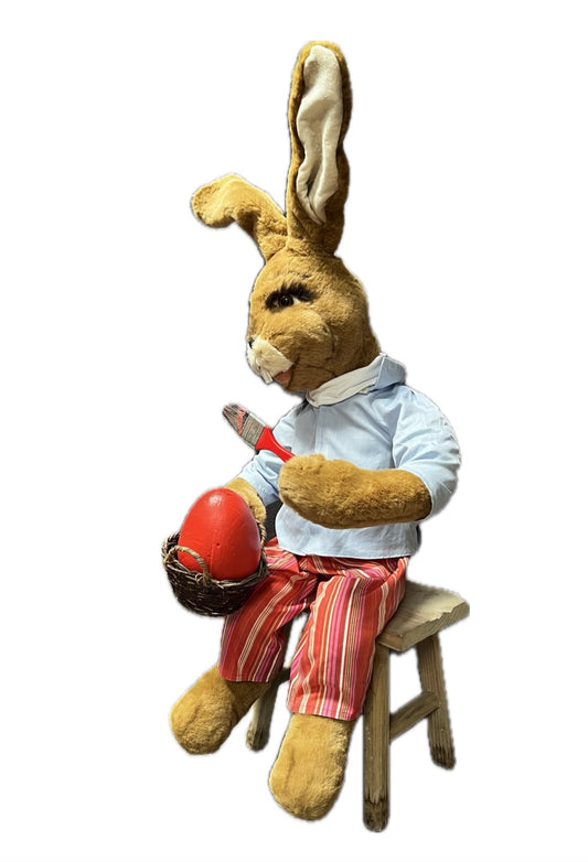 Hase sitzend mit Pinsel malt Ei rot an